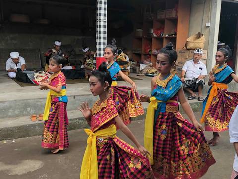 Young Balinese dancers in gold and pink costume performing at a village temple.