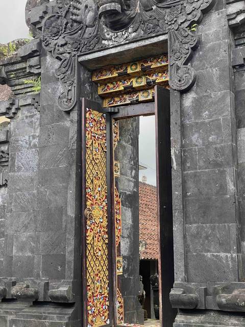A carved stone temple gate in Sidemen, its wooden door painted red and gold, standing open.