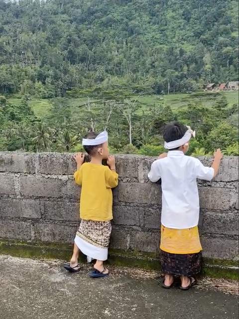 Two boys in temple dress lean on a wall above the Sidemen rice fields, looking out across the valley.